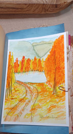 A watercolor painting of an autumn landscape with orange and yellow trees, a winding path, a white lake or field, and muted green mountains in the background, photographed on green paper.