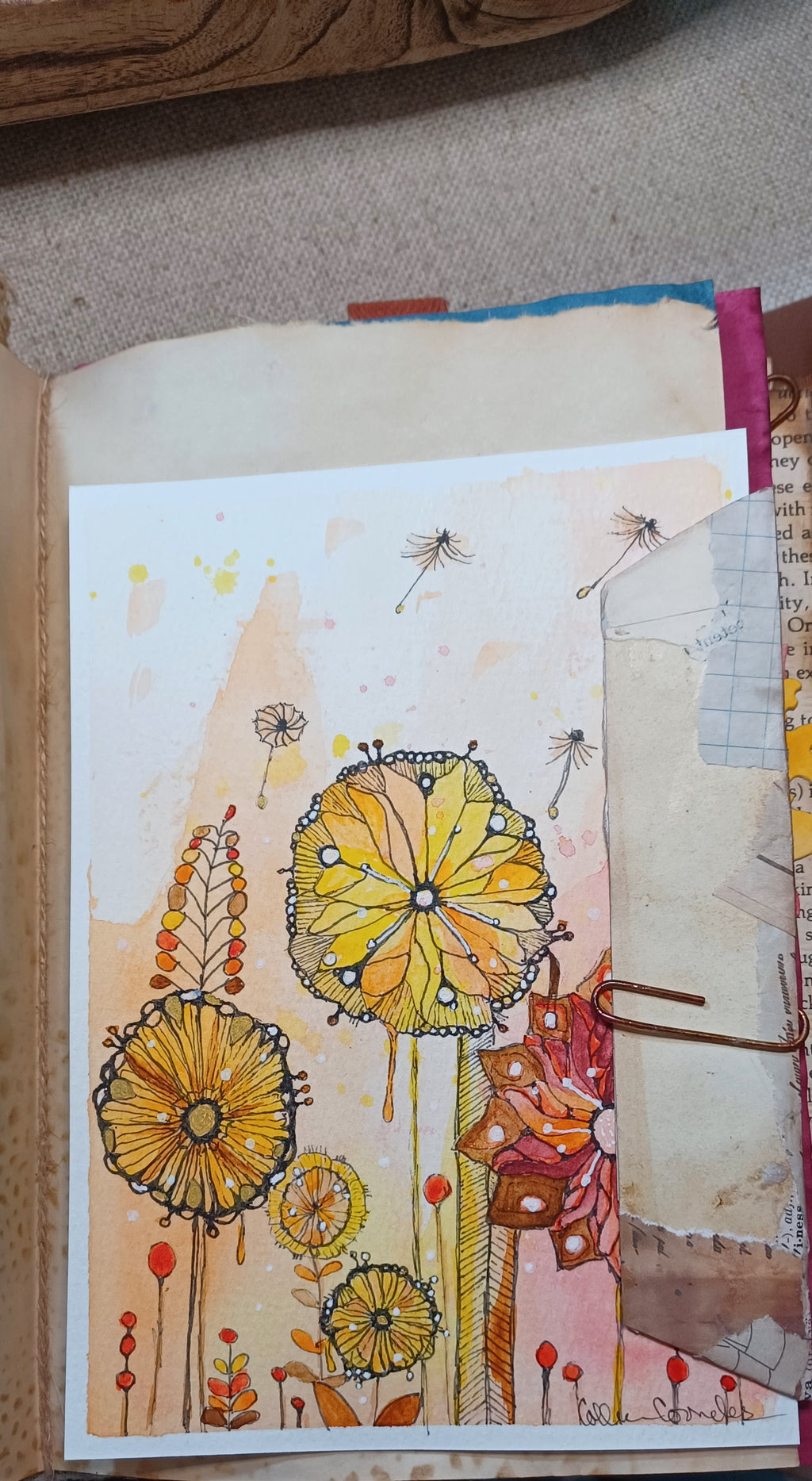 A handmade art journal page featuring whimsical watercolor flowers in yellow, orange, and red, alongside layered paper tabs and a metal binder clip.