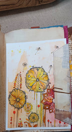 A handmade art journal page featuring whimsical watercolor flowers in yellow, orange, and red, alongside layered paper tabs and a metal binder clip.
