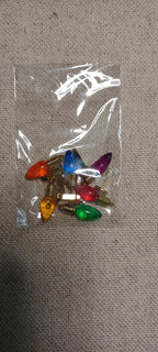 A small clear plastic bag containing several colorful Christmas light bulbs with gold brad base , placed on a beige fabric background.