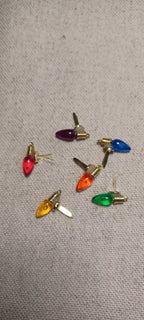 A set of seven Christmas light-shaped paper fastener with gold brad base in red, purple, blue, orange, green, yellow, and white, arranged on a beige textured fabric background.
