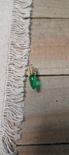 A small green teardrop-shaped paper fastener with gold brad base, placed on a rustic wooden surface next to a white fringed textile.