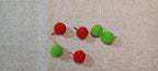 six small felt pom-pom decorative paper fasteners , alternating red and green, arranged on a textured beige linen fabric background.