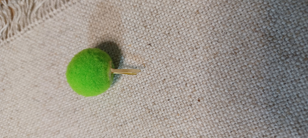 A bright green felt pom-pom decorative paper fasteners , resting on a textured beige linen fabric background.
