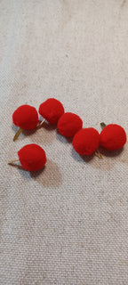 Five small red pom-pom Paper Fastener with gold-tone wire stems, arranged on a textured beige fabric background.