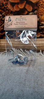 Packaged assorted blue and white cabochon decorative paper fasteners with patterns that vary by set