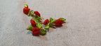 A pair of handmade rose decorative paper fasteners made from rolled red fabric petals with green ribbon leaves, displayed on a textured beige linen background.