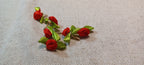 A pair of handmade red ribbon rose decorative paper fasteners with green ribbon leaves, displayed on a textured beige linen fabric background.