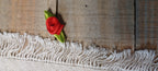 A small embroidered red rose with green leaves decorative paper fasteners on a rustic wooden surface above a white fringed textile.
