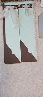 A pair of decorative paper bookmarks with a pale mint green and dark brown color-blocked design, featuring white polka dots, lace ribbons, and a small photo strip at the top, displayed on a beige textured fabric background.