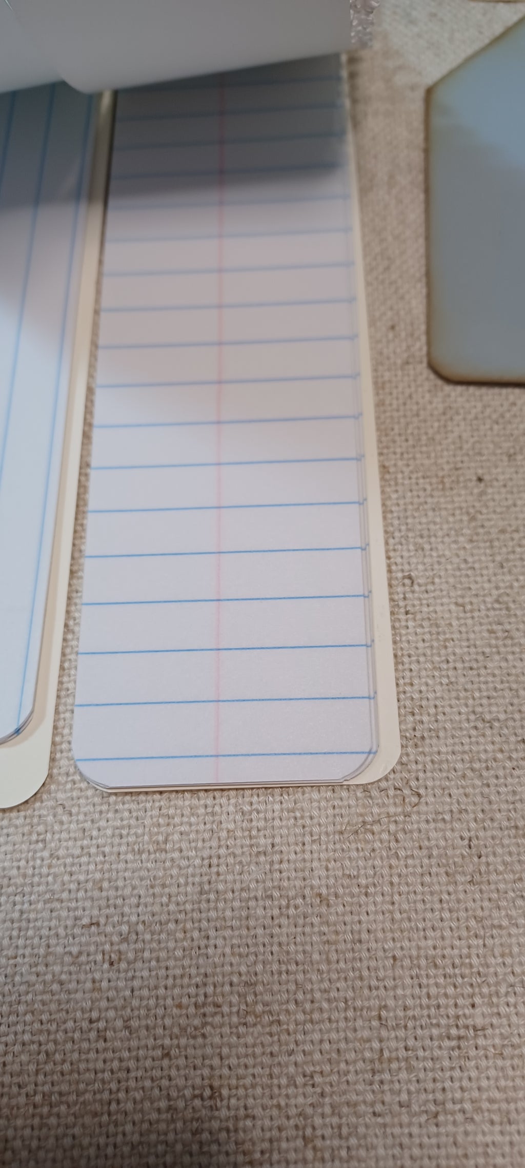A close-up of lined paper notepad pages with blue and red lines, partially visible on a beige woven fabric surface.