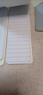 A close-up of lined paper notepad pages with blue and red lines, partially visible on a beige woven fabric surface.