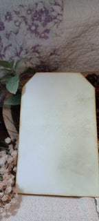 A blank, off-white rectangular card or sign with rounded corners, displayed on a textured fabric surface next to dried flowers and a floral-patterned background.