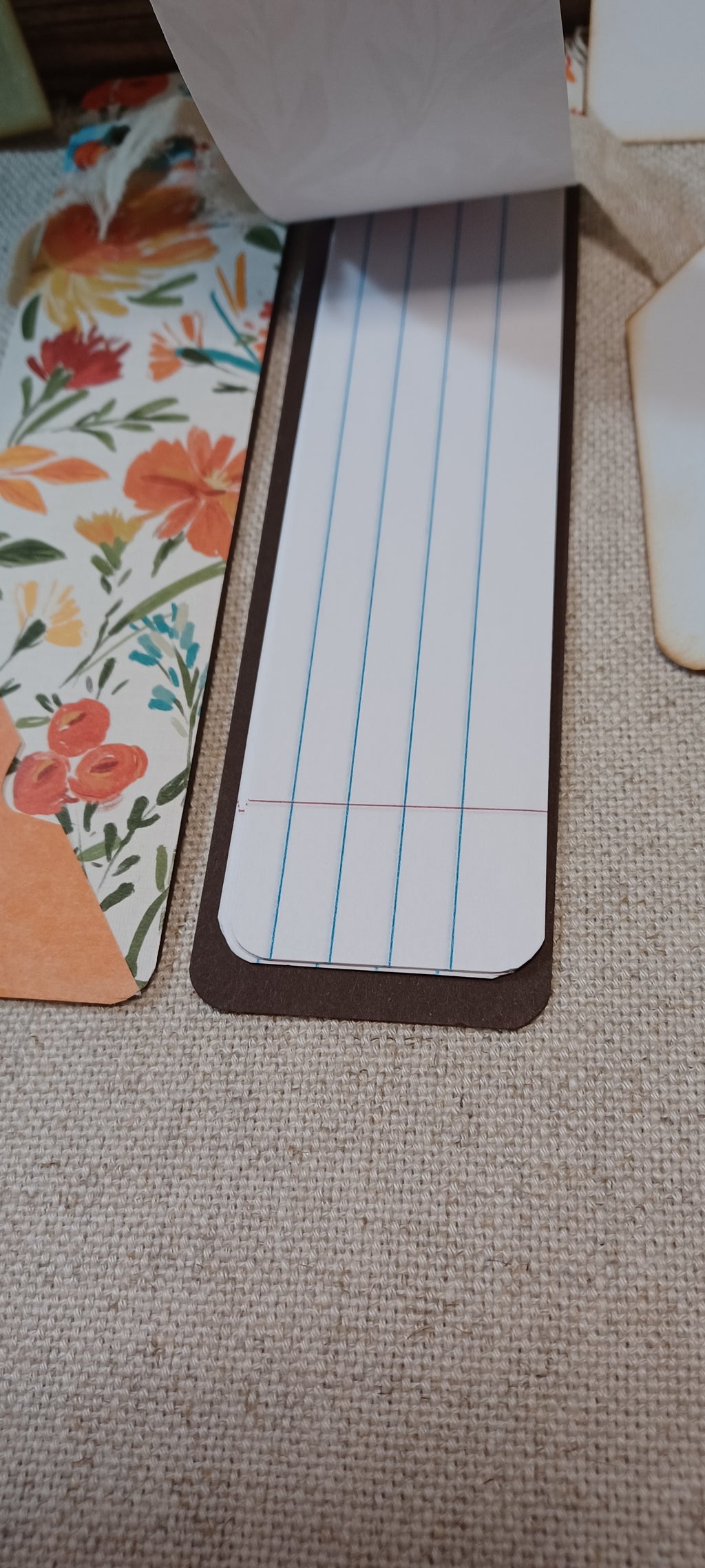 A close-up of a lined notepad sheet with blue and red lines, placed on a textured beige fabric surface next to a floral-patterned item.