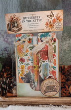 Autumn Treasures Mini Journal Kit in its packaging, featuring a butterfly-themed cover with colorful floral patterns, a burlap ribbon, and a round sticker that reads 'The Hidden Drawer'.