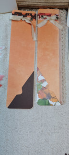 Two decorative paper bookmarks with orange panels, floral patterned accents, and ribbon bows, laid on a light fabric surface.