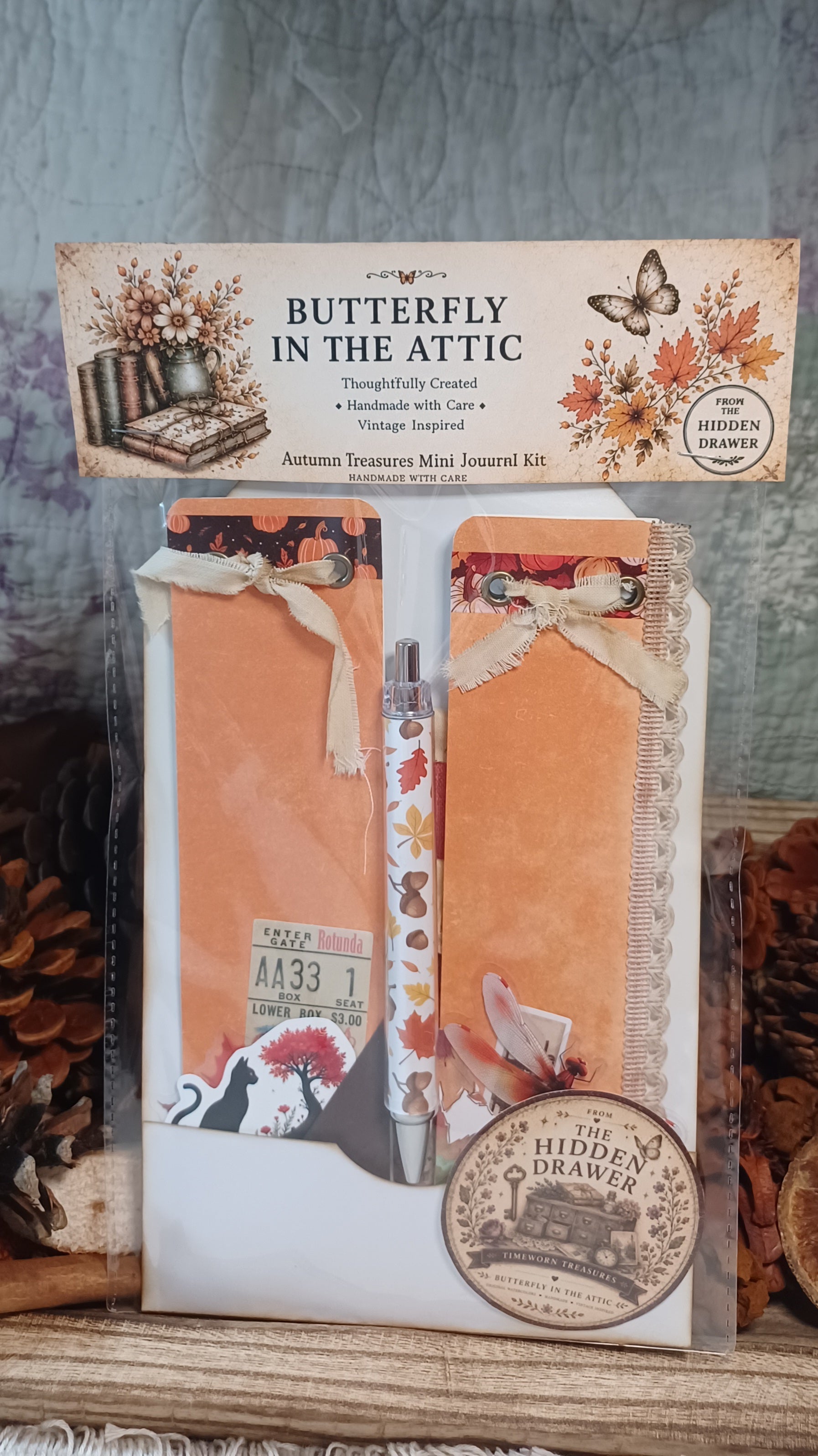 Autumn Treasures Mini Journal Kit in 'Butterfly in the Attic' theme, featuring orange paper, vintage-style labels, a butterfly-themed pen, and decorative ribbons, packaged in a clear sleeve with a printed header card.