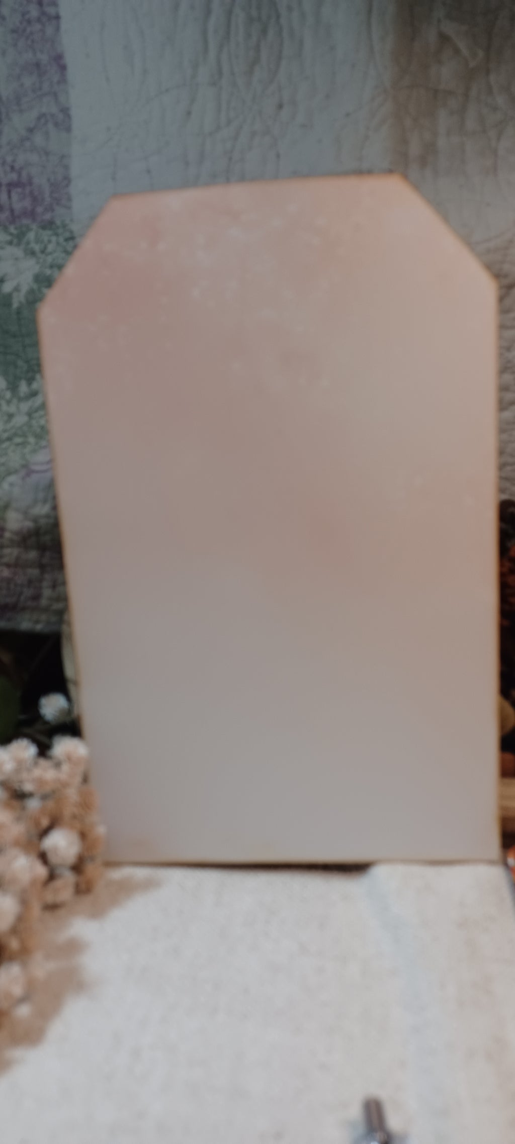 A blank, light beige or pale pink rectangular board with a notched top edge, standing upright on a textured white surface.
