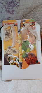 A decorative pen with a clear barrel and silver accents, resting on a white envelope decorated with autumn-themed paper collage, sunflowers, and dried flowers.