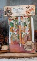 Butterfly in the Attic Autumn Treasure Mini Journal Kit in its clear plastic packaging, featuring vintage-style autumn illustrations, a pen, and a hidden drawer insert, displayed on a rustic wooden surface with pinecones.