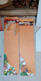 Two handmade paper bookmarks with autumn-themed designs, featuring a solid peach-orange center with printed fall leaves and pumpkins near the top and bottom, laid flat on a textured fabric surface.