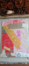 A mixed-media collage art piece featuring textured paper strips in pink, red, yellow, brown, and blue, styled on a neutral fabric surface with pinecones at the top.