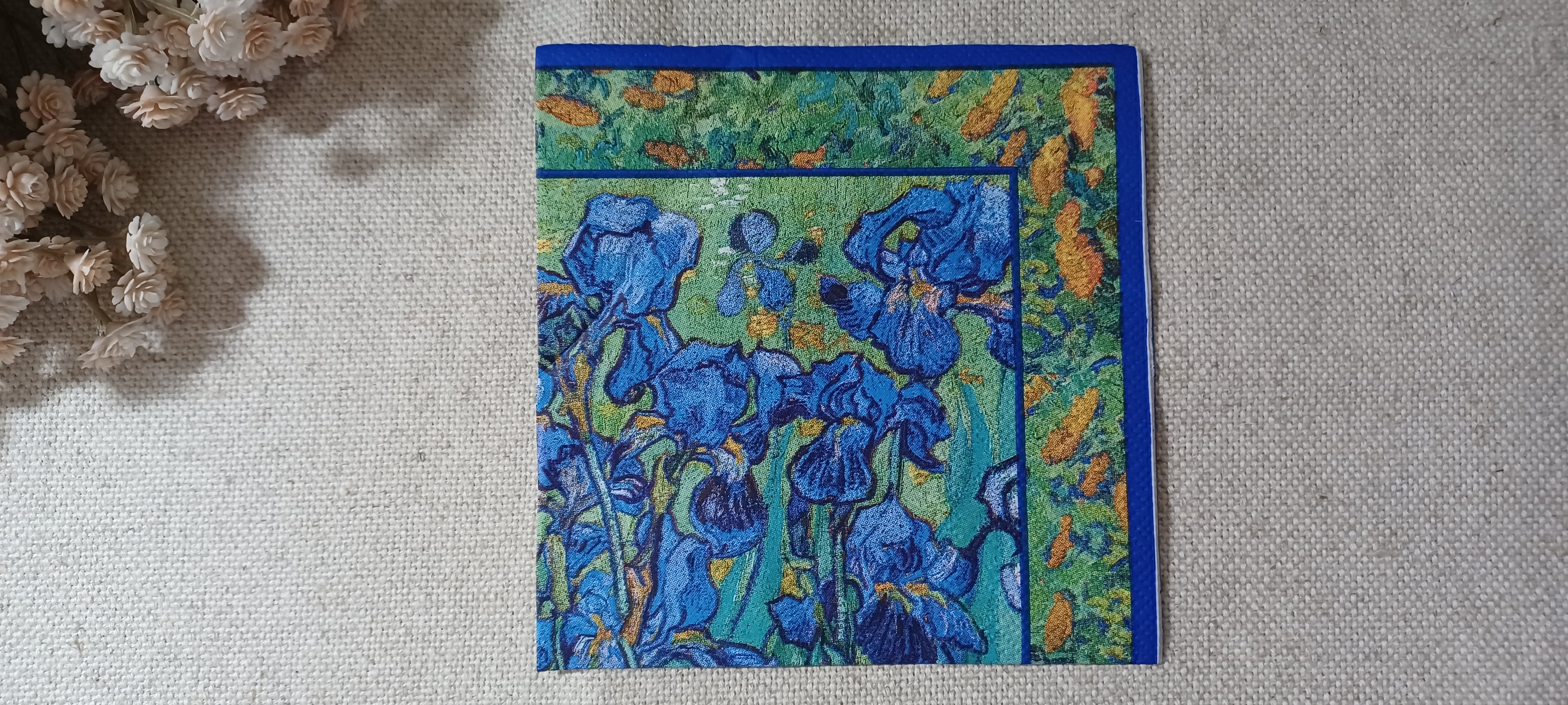 Decorative cocktail napkin with blue iris flowers, turquoise green background and deep blue border.