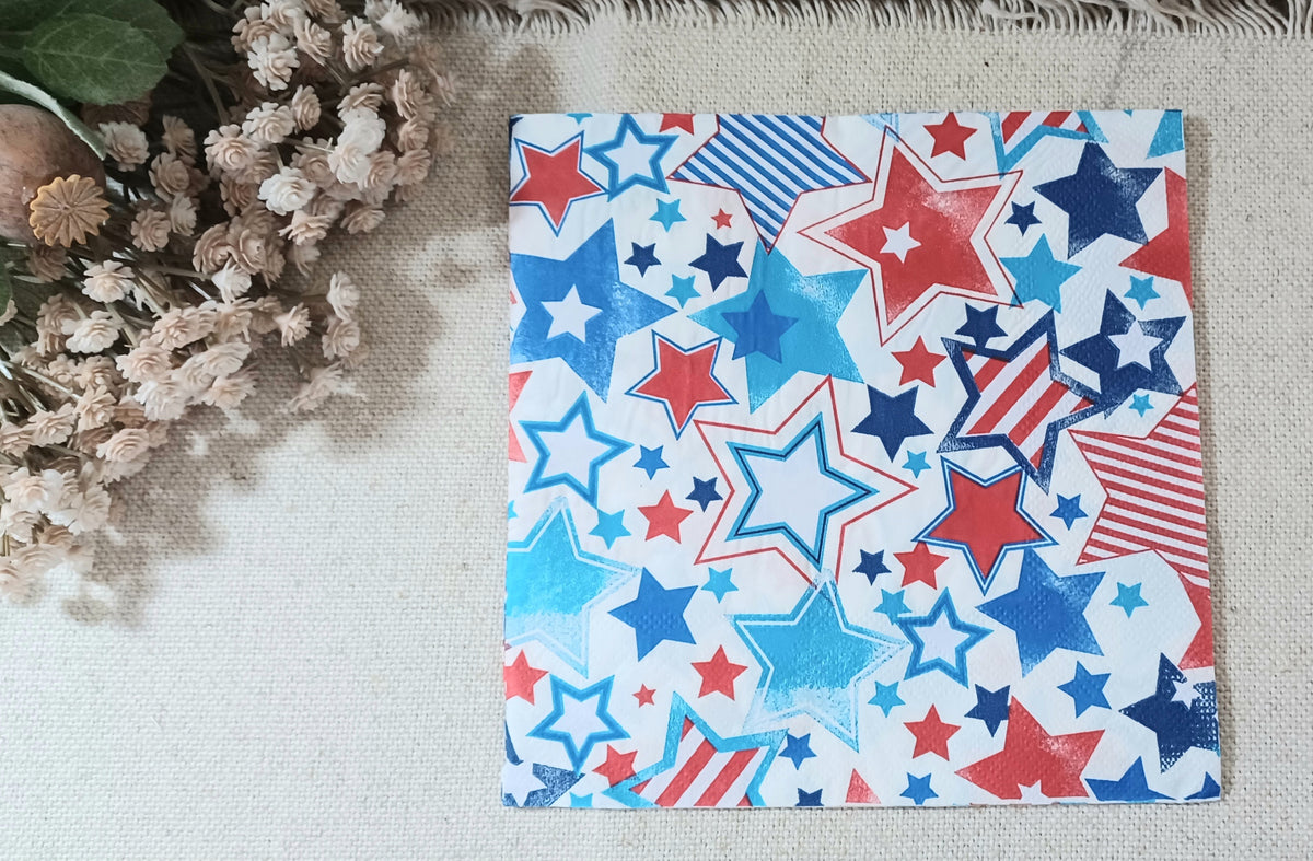Single decorative paper napkin with assorted red, white, navy and bright blue stars in solid, striped and outlined patterns.