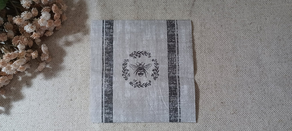 Black bee and botanical wreath cocktail paper napkin on a gray linen-look background for decoupage, junk journals and collage crafts.