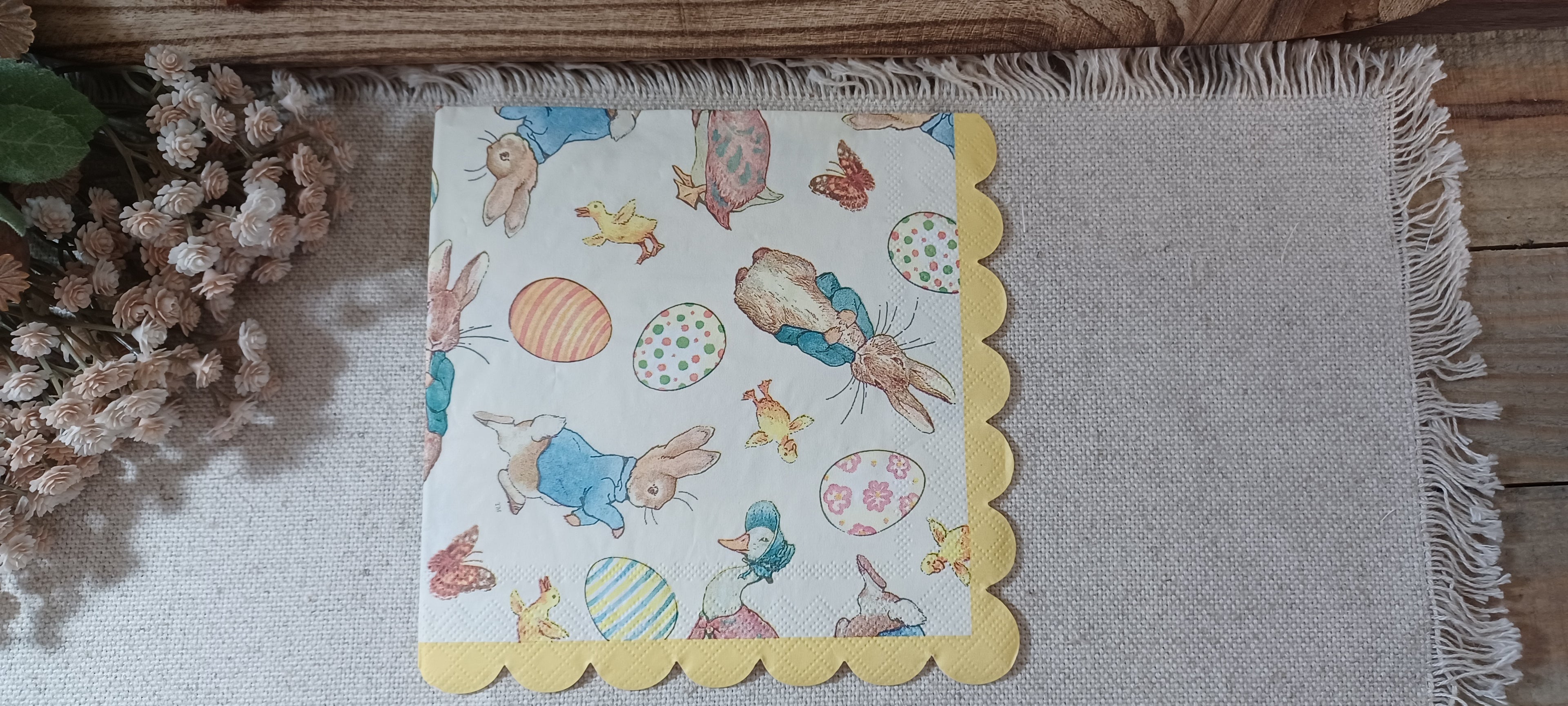 Luncheon-size Easter paper napkin featuring storybook rabbits, decorated eggs, chicks, ducks and a yellow scalloped border.