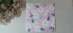A square pink paper napkin with a white daisy floral pattern, displayed on a beige textured fabric surface next to dried flowers. Great for crafts