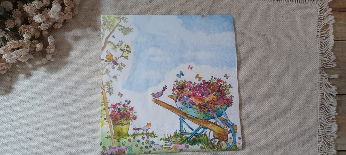 Garden wheelbarrow floral paper napkin with colorful flowers, birds, butterflies, blue sky, and gardening tools.