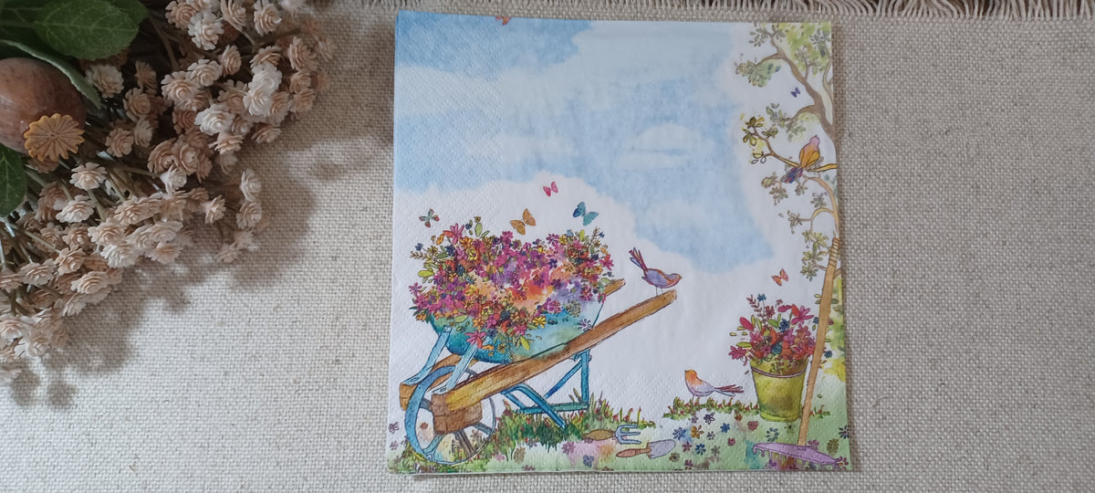 Opened garden paper napkin showing the flower-filled wheelbarrow, birds, butterflies, garden tools, and watercolor sky in the opposite orientation.