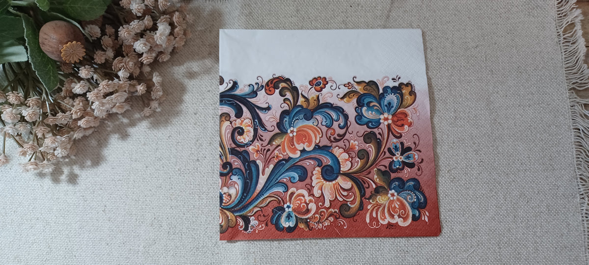 Norwegian rosemaling folk art paper napkin with ornate blue, coral, cream, and brown floral scrollwork on a rose background.