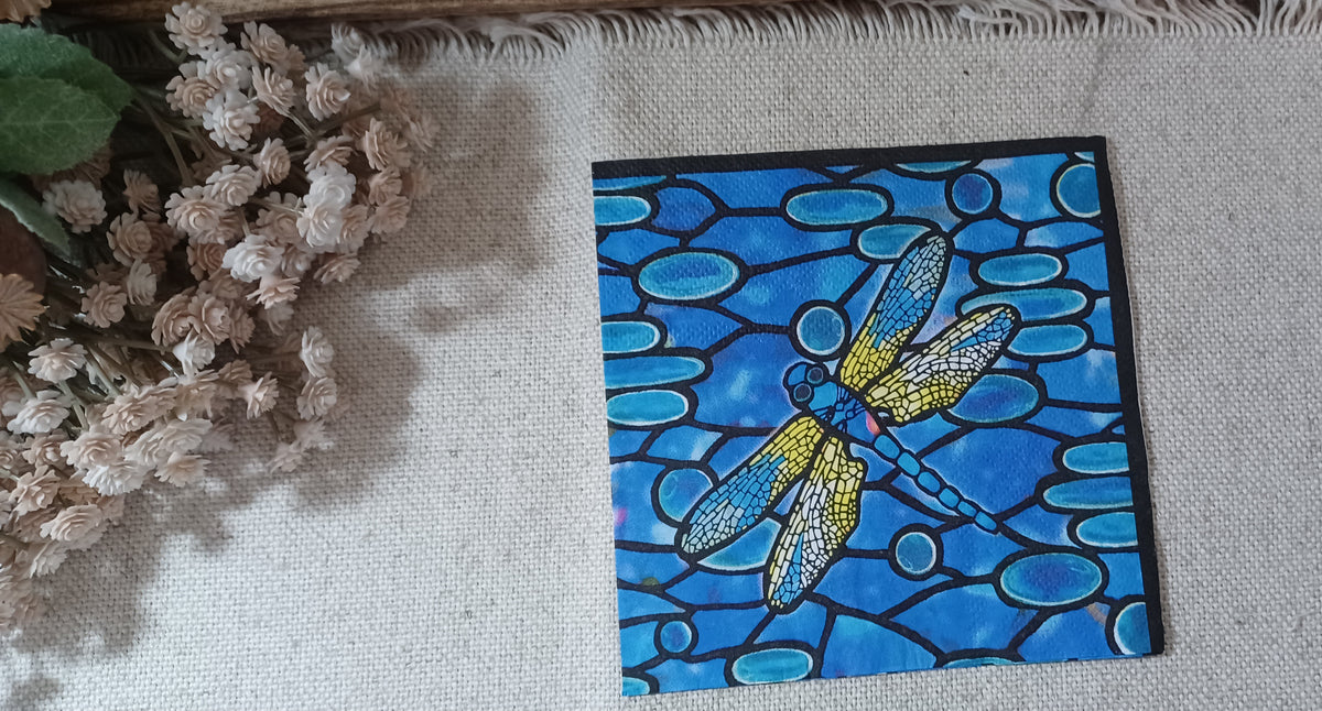 Blue stained glass dragonfly paper napkin with a yellow, white and turquoise dragonfly over a cobalt blue mosaic pattern.