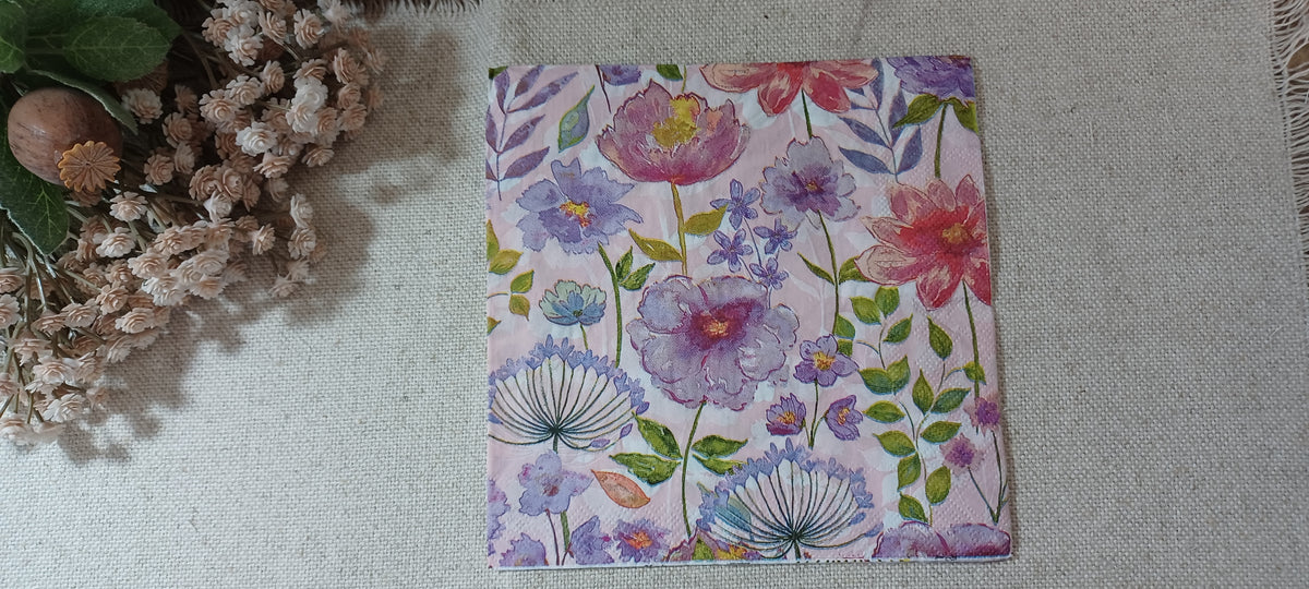 Close view of pink and purple watercolor flowers with green leaves on a pale pink paper napkin.
