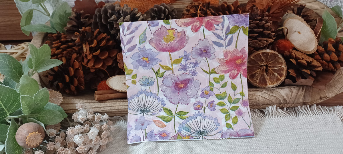 Watercolor floral decoupage napkin with pink, lavender and blue garden flowers displayed in a rustic botanical setting.