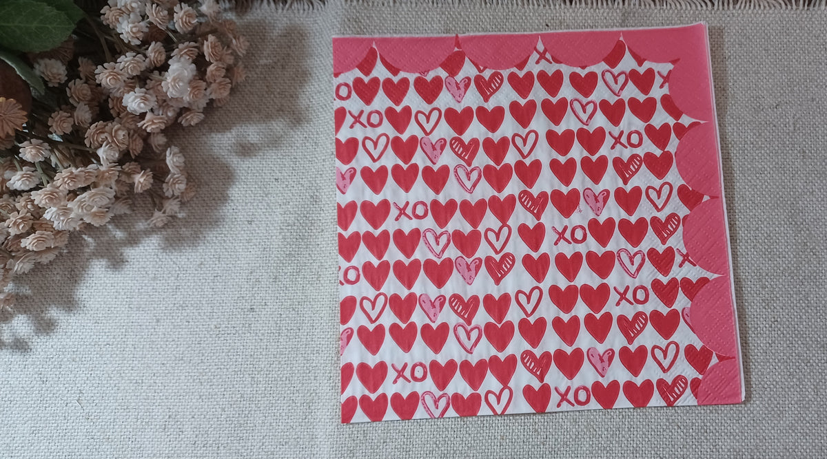 Red and pink heart paper napkin with XO details and a pink scalloped border on a white background.