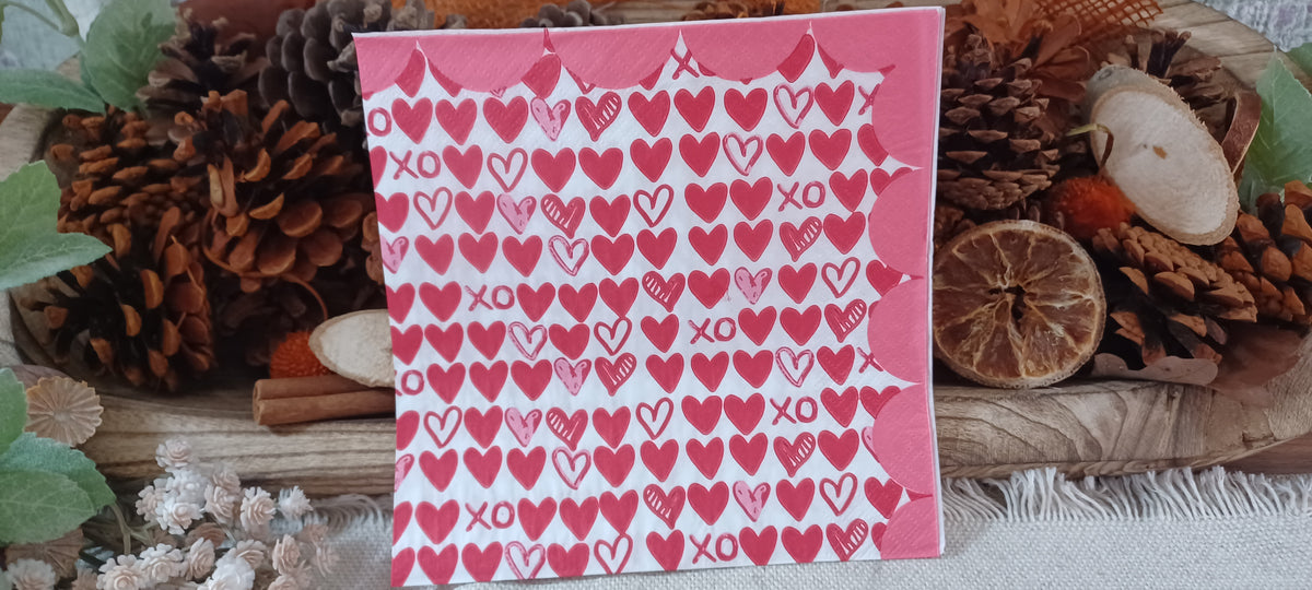 Close view of red and pink hearts and XO pattern on a white paper napkin with pink scalloped edging.