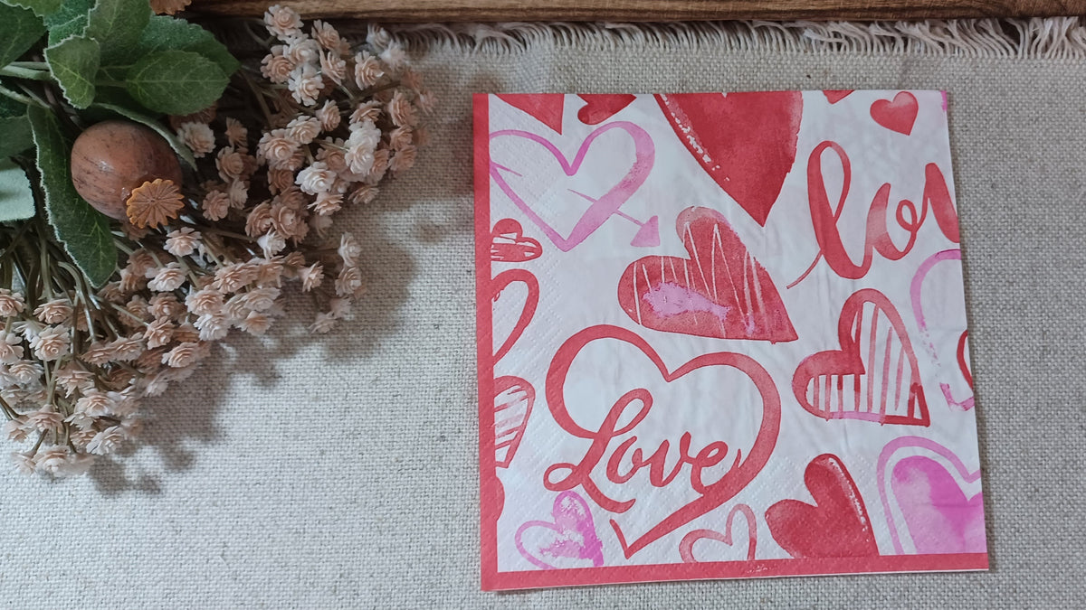 Red and pink watercolor heart paper napkin with handwritten Love lettering on a white background.