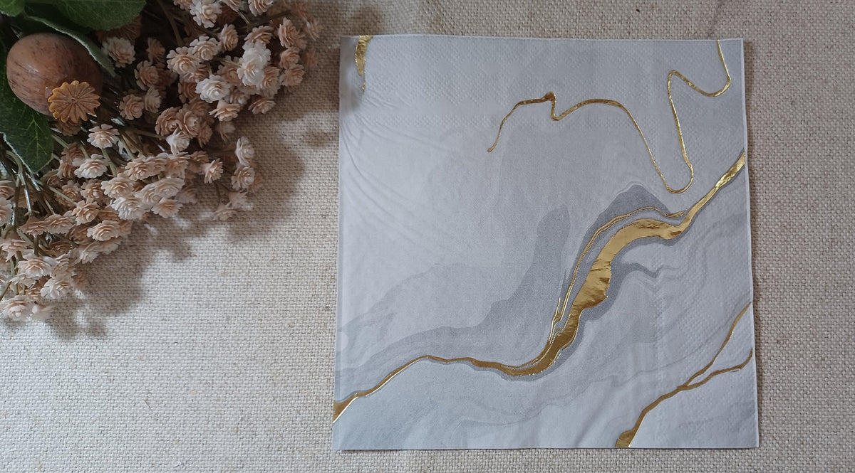 White and gray marble luncheon napkin with metallic gold foil accents displayed with rustic botanical decor.