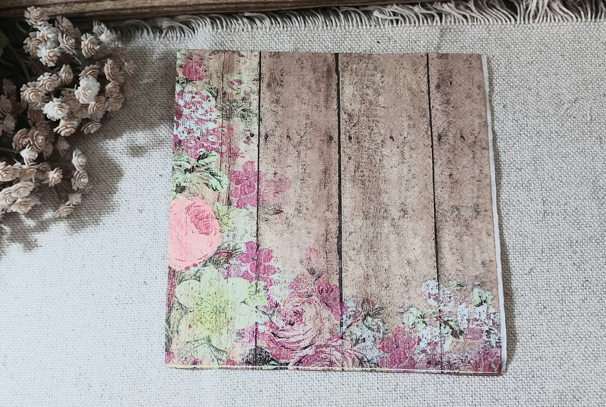Rustic wood plank luncheon napkin bordered with distressed pink roses and muted green foliage.