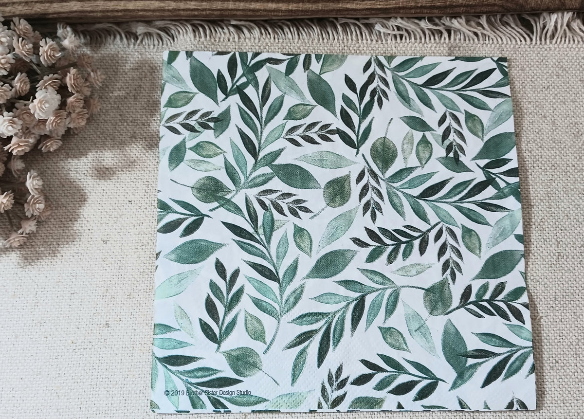 Green botanical paper napkin with watercolor-style leafy branches in varied shades of green on a white background.