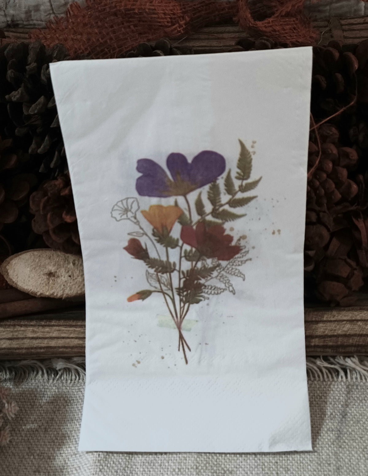Pressed wildflower bouquet guest napkin displayed upright against a rustic woodland background.
