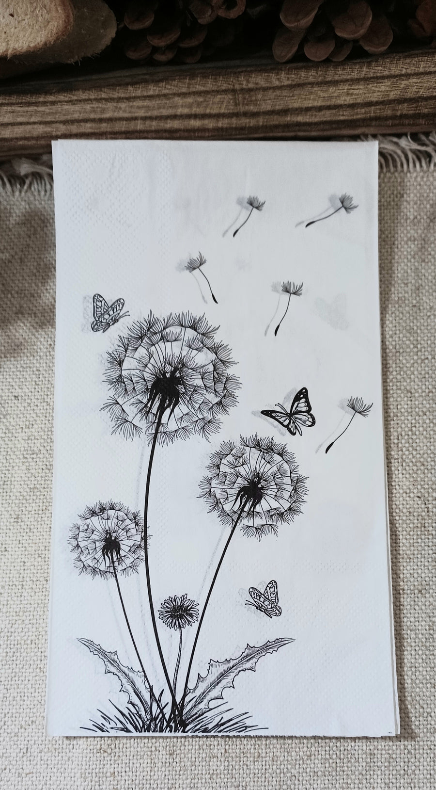 Black and white paper guest napkin featuring illustrated dandelions, floating seeds and butterflies.