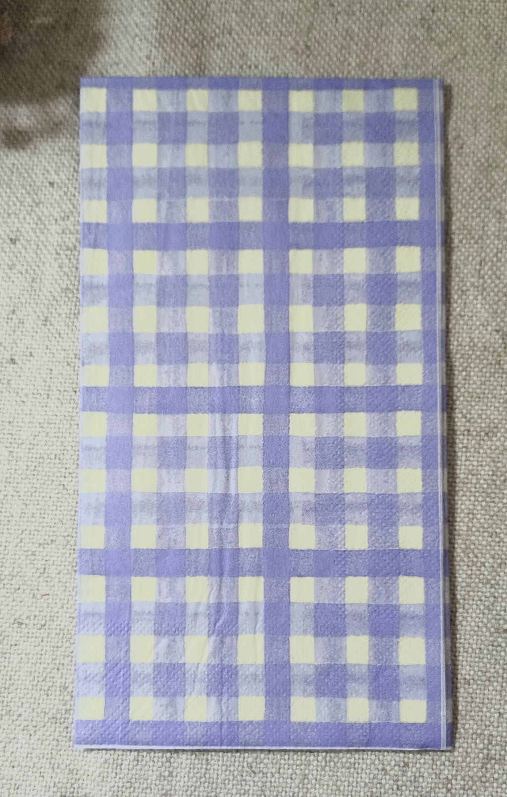 Lavender purple and creamy white gingham check paper guest napkin shown flat on a neutral fabric background.