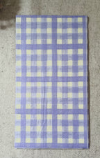 Lavender purple and creamy white gingham check paper guest napkin shown flat on a neutral fabric background.