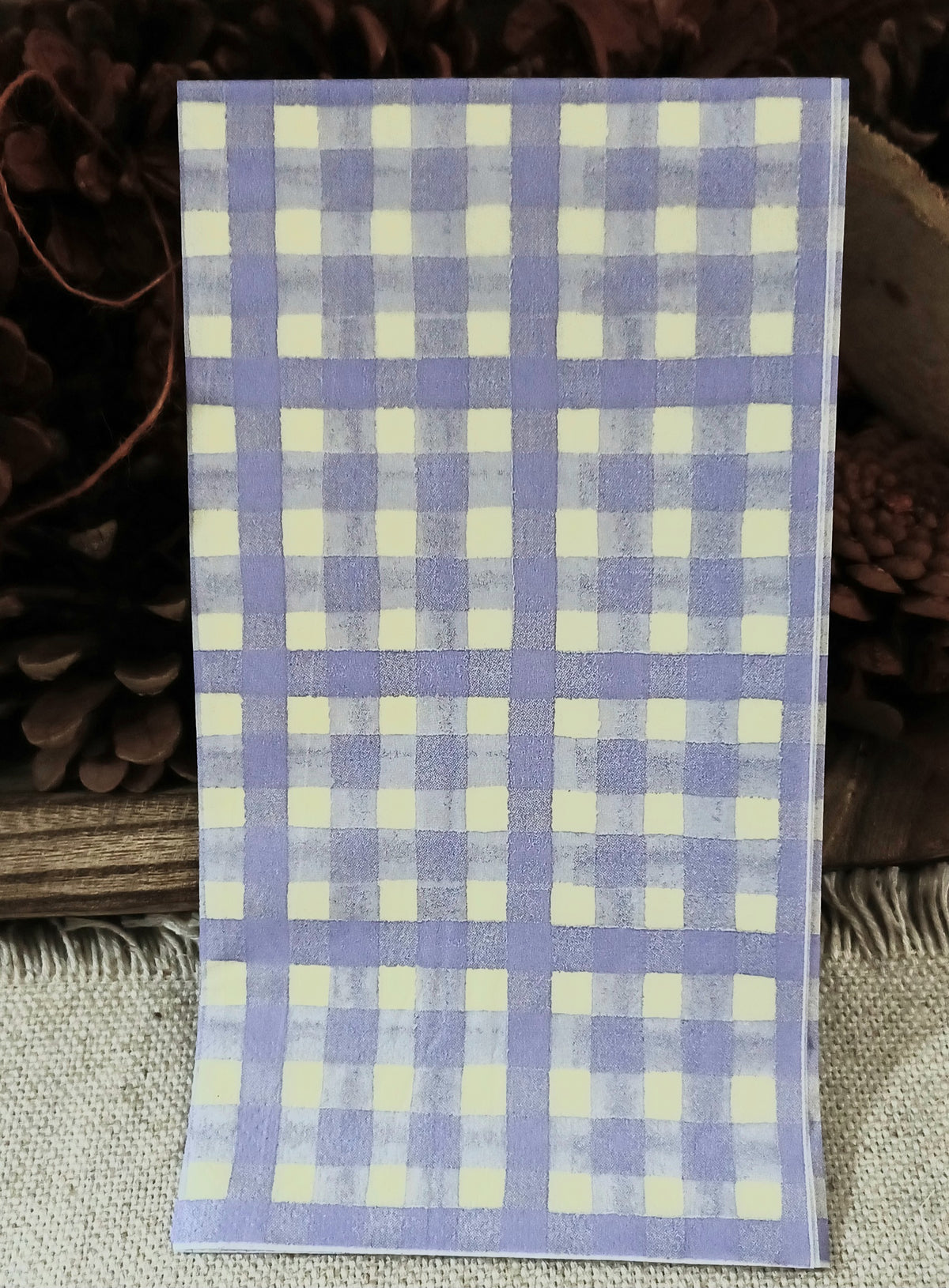 Lavender gingham paper guest napkin with a repeating purple and cream checkered pattern displayed with rustic styling