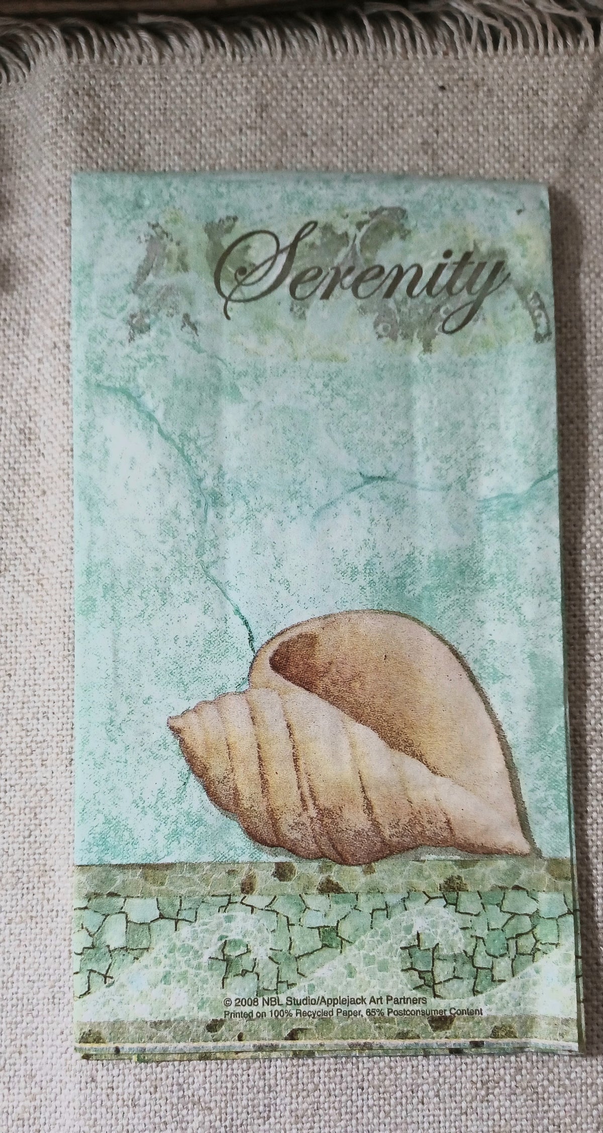 Aqua vintage-style coastal paper guest napkin featuring a large seashell, distressed textures, and the word Serenity in script.