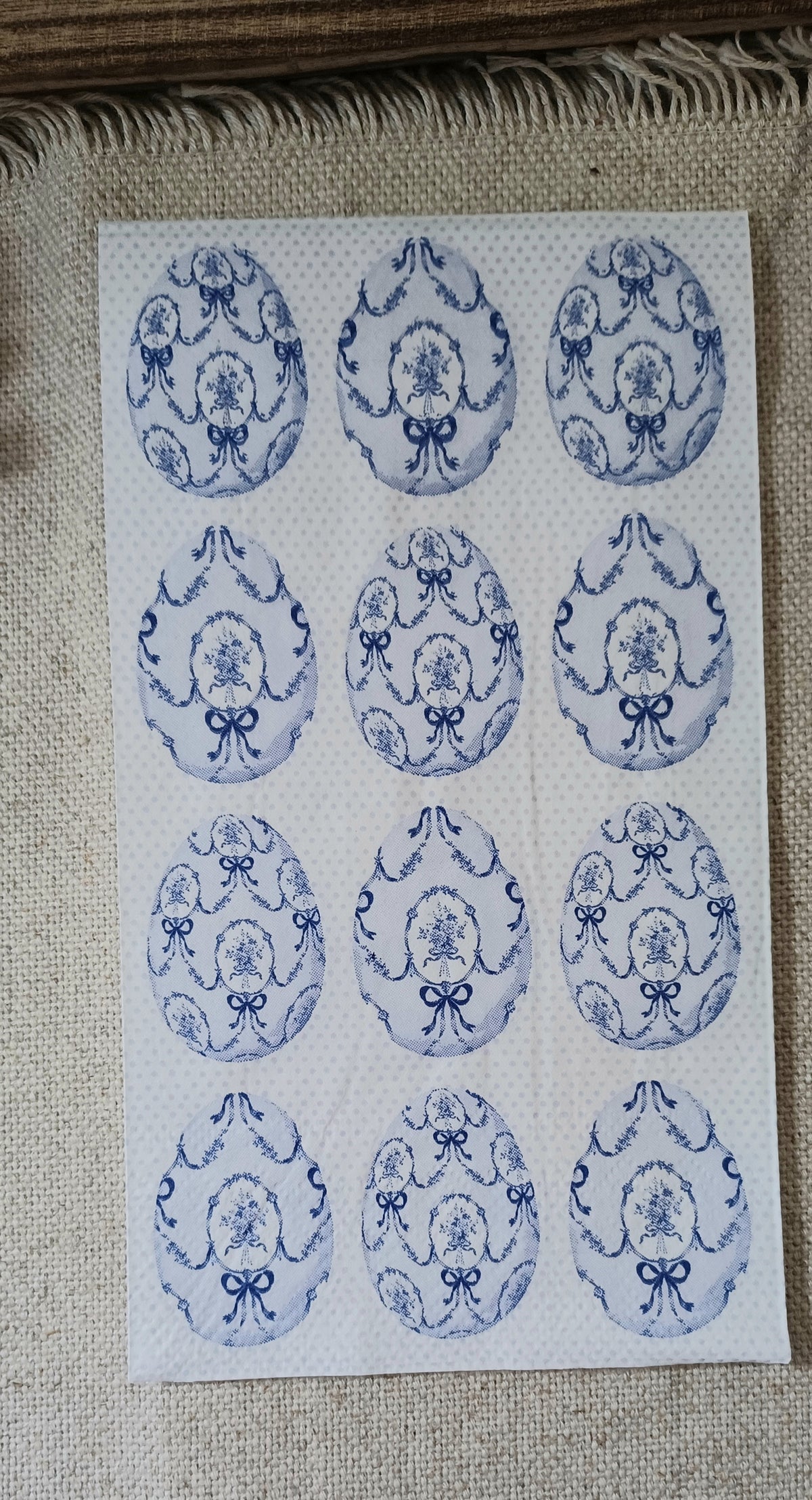 Styled blue toile guest napkin featuring repeating floral medallions and ribbon bows displayed against rustic natural decor.